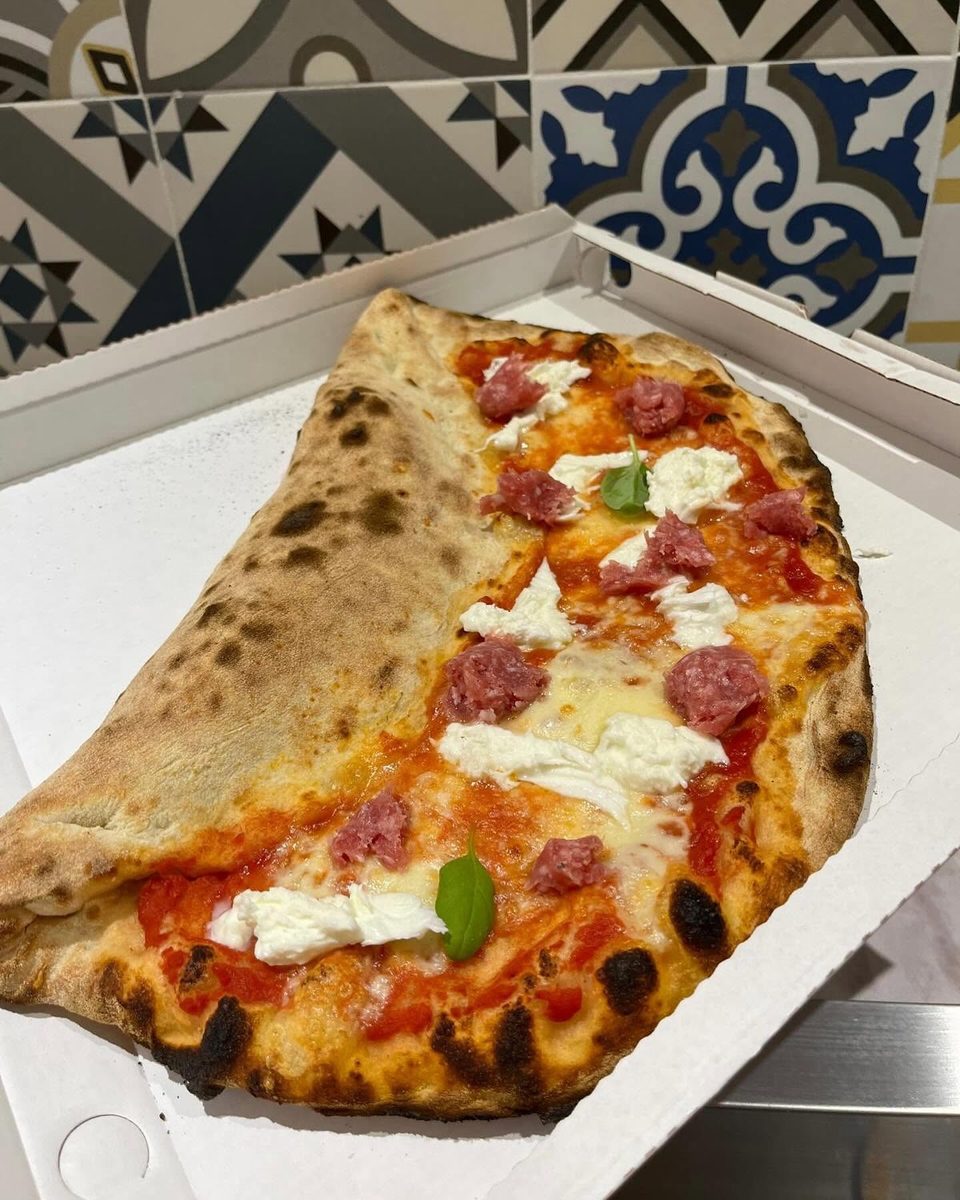La pizza Duchessa: mezzaluna col bordo ripieno, salsiccia e bufala, davanti alle piastrelle blu del banco